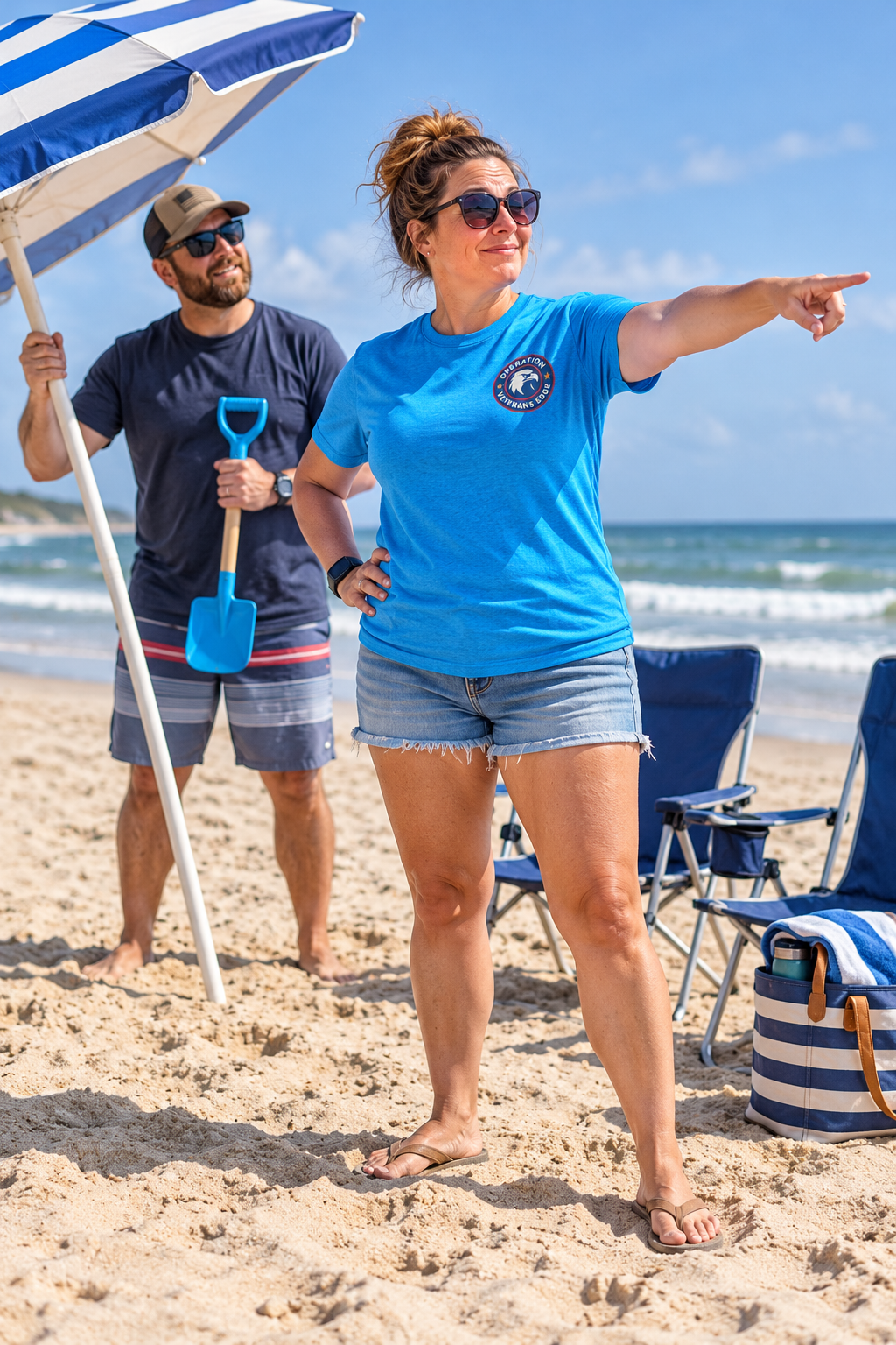 Illustrative lifestyle mockup: white woman in a turquoise OVE tee directing placement of a beach umbrella.